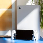 Ein PS Portal steht an eine PS5 gelehnt auf einem blauen Tisch.