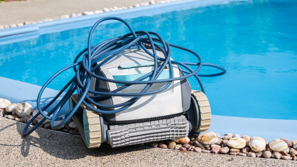 Ein Poolroboter mit aufgewickeltem Schlauch auf ihm steht am Rand eines Schwimmbeckens.