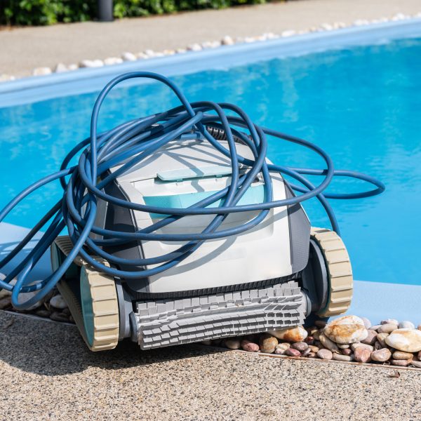 Ein Poolroboter mit aufgewickeltem Schlauch auf ihm steht am Rand eines Schwimmbeckens.